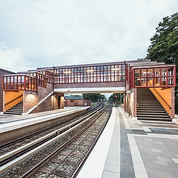 Eine moderne Brücke aus Stahl und Ziegel mit großen Fenstern, die über Gleise führt.