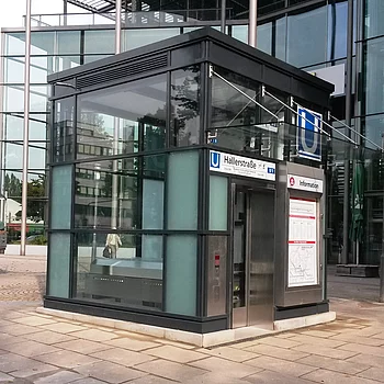 Moderne U-Bahn-Station mit Glaswänden und schwarzem Dach.