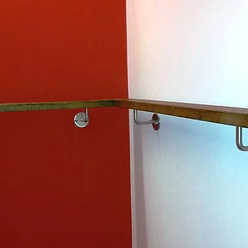 Holzhandlauf mit Metallhalterungen, an einer Wand mit roter Farbe montiert.