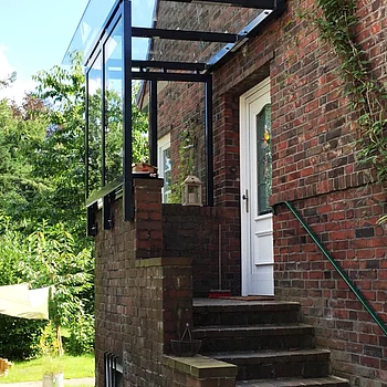 Vordachkonstruktion aus Glas und schwarzem Metall über einer Treppe, die zu einer weißen...